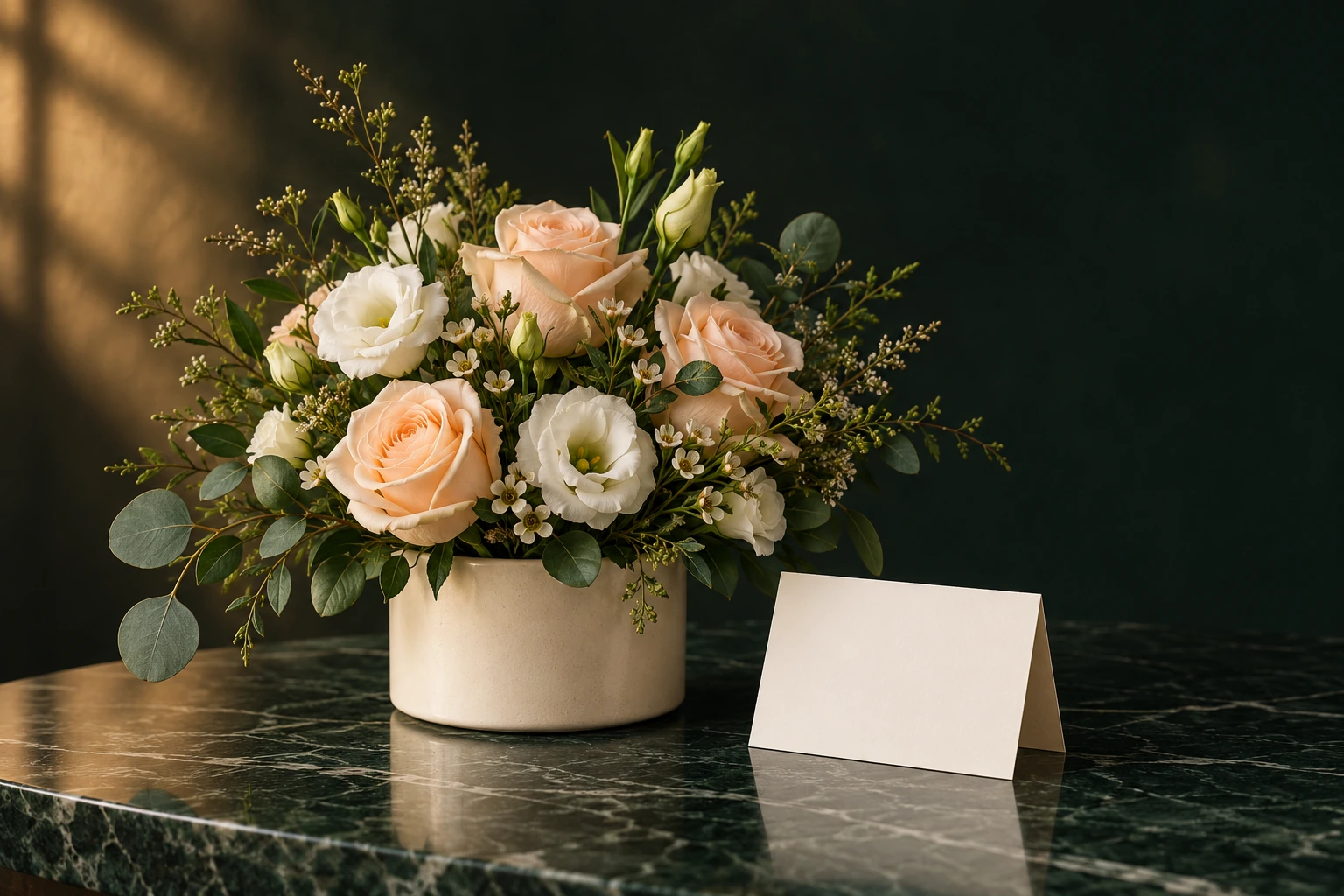 A compact peach and white flower arrangement in an ivory container beside a blank card on green marble